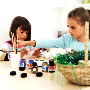 Two Girls (6-8) Painting Easter Eggs on a Table 