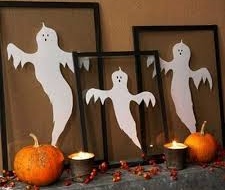 Three framed ghosts, pumpkins and candles on a table