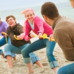 a group of people playing tug of war with a yellow rope on the beach